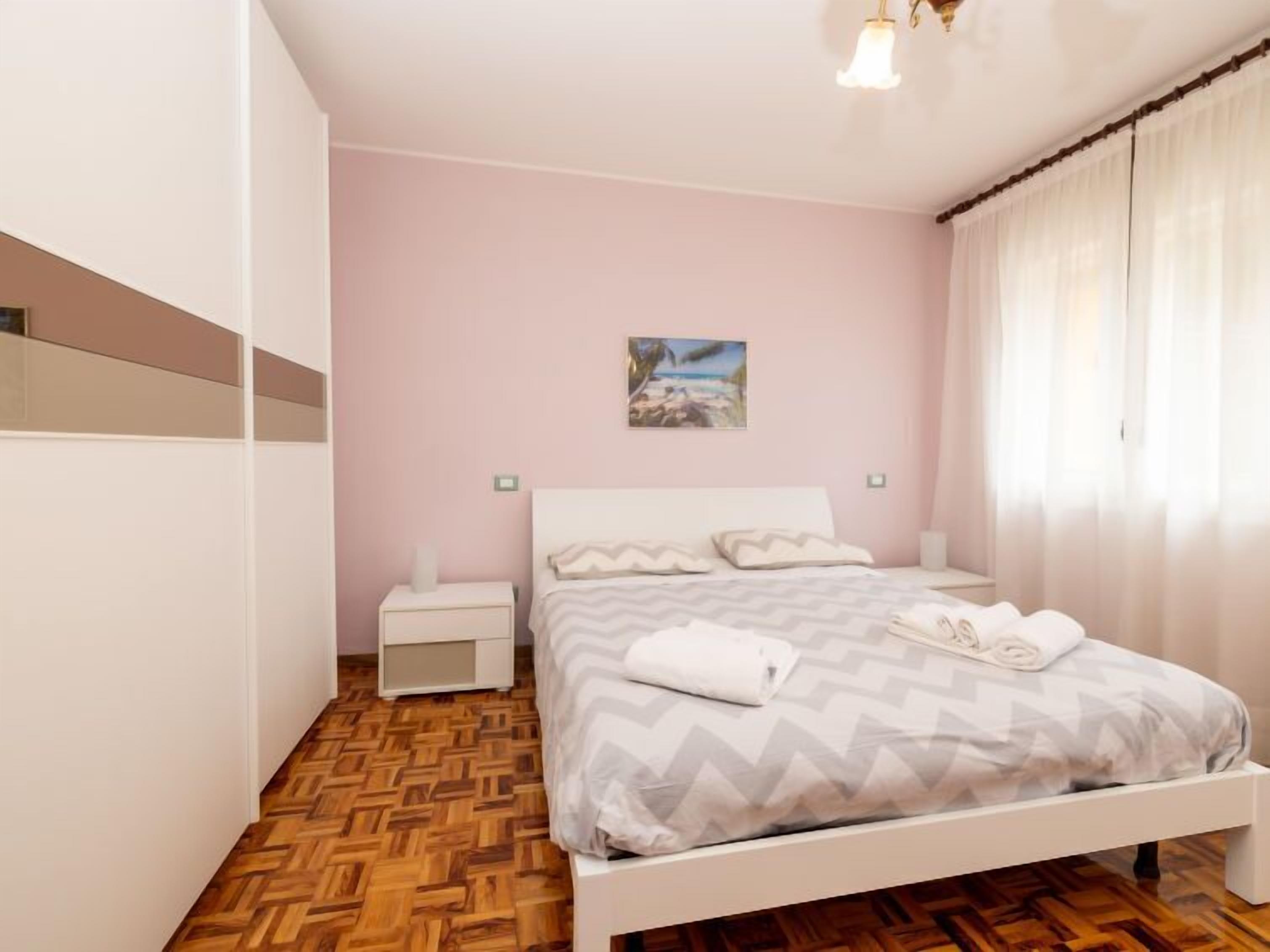 A bedroom with a bed, nightstands, a painting, and a wooden parquet floor.