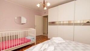 A bedroom with a crib, a bed with rolled towels, a mirror, and a wardrobe. - La Corleta di Sora by Interhome (Ovaro)