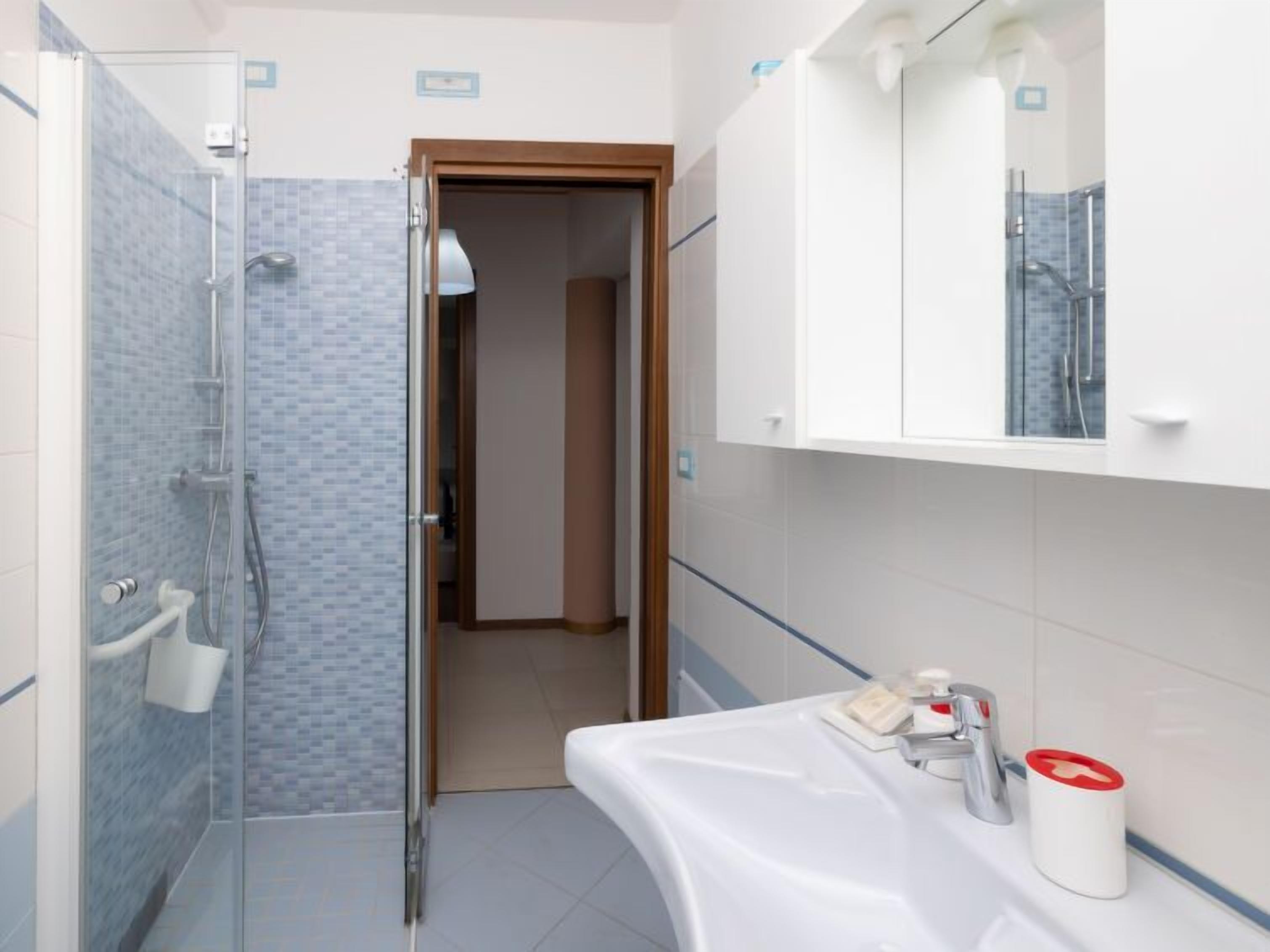 Une salle de bain moderne avec une douche à parois de verre, un lavabo blanc doté d’un distributeur de savon rouge et un miroir au-dessus du lavabo.