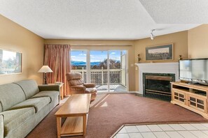 Ein Wohnzimmer mit einer Couch, einem Holztisch, einem Fernseher, einem Kamin und einem Balkon mit Blick.