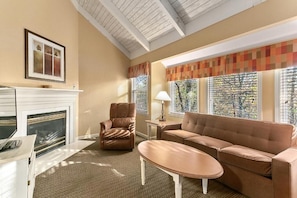 A living room with a fireplace, a sofa, a chair, and a table. - Pigeon Forge | Family Smoky Getaway | Pool + Hot Tub | 2BR (Pigeon Forge)