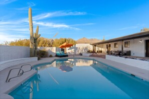 Une piscine, un ciel bleu dégagé, un cactus et un bâtiment doté d’une terrasse.