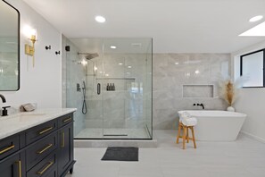 Une salle de bain moderne dotée d’une douche à parois de verre, d’une baignoire sur pieds et d’un meuble-lavabo avec des poignées dorées.