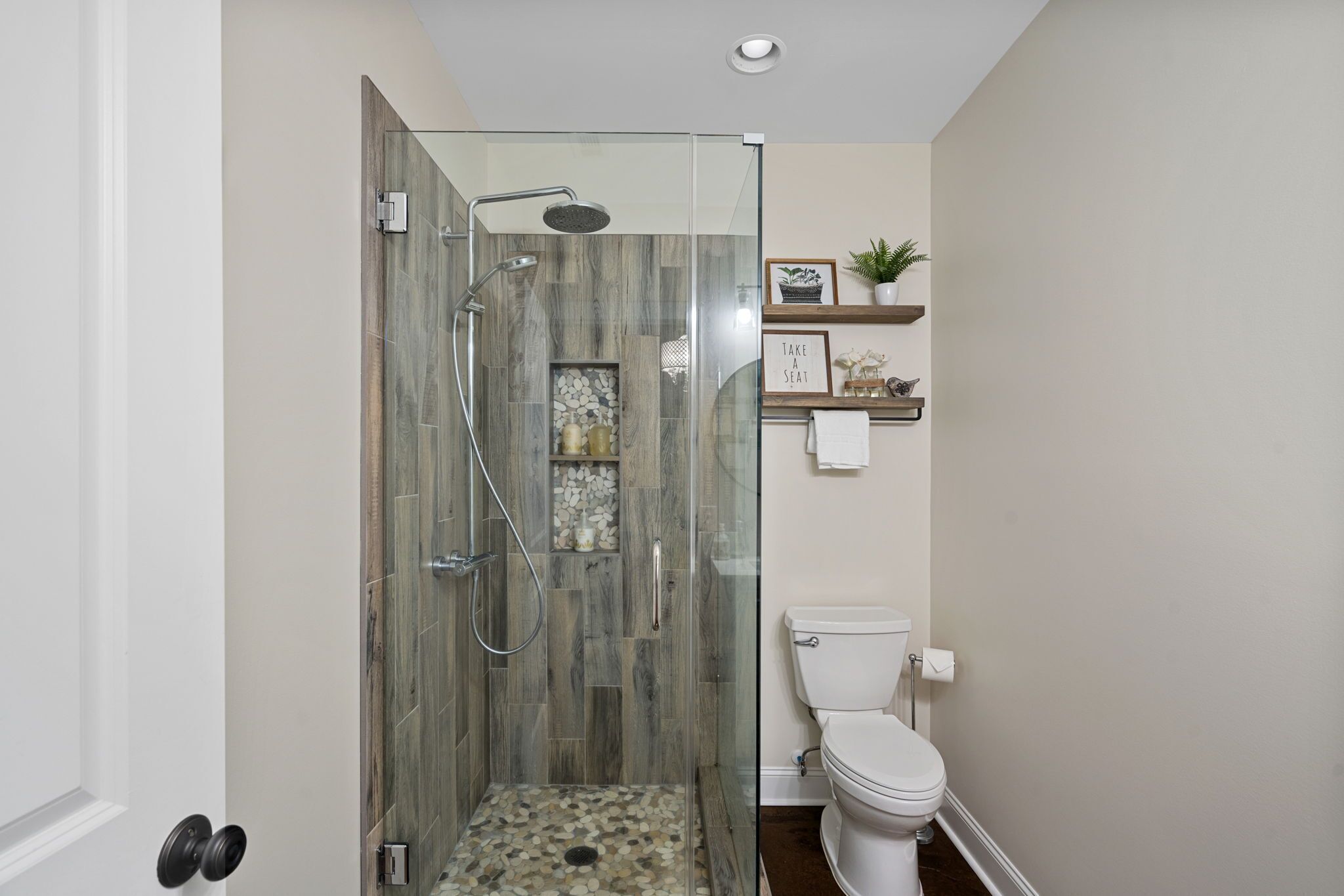 A modern bathroom with a glass-enclosed shower, a toilet, and a shelf with decorative items.