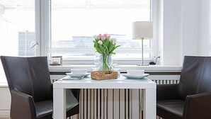 En spiseplads med et hvidt bord, to sorte stole, en vase med blomster og en lampe.