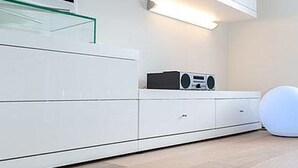Et moderne værelse med et hvidt skab, en glashylde, en hvid stol og en hvid lampe.