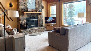 A cozy living room with a stone fireplace, a television, and a large window offering a view of the outdoors. - Riverfront Hot Tub & Starlink - South Platte Frontage, 15mi to Breck (Alma)