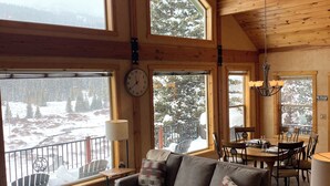 A cozy cabin interior with a wooden ceiling, large windows, a dining area, and a living room with a sofa and ottoman. - Riverfront Hot Tub & Starlink - South Platte Frontage, 15mi to Breck (Alma)