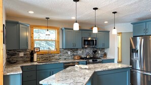 A modern kitchen with teal cabinets, granite countertops, stainless steel appliances, and pendant lighting. - Riverfront Hot Tub & Starlink - South Platte Frontage, 15mi to Breck (Alma)