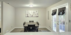 A dining area with a table and chairs, a ceiling light, a painting on the wall, and a door with curtains.