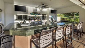 Ein moderner Außenbereich mit Bar, Pool, Barhocker und Deckenventilator.