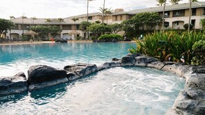 Ein Pool mit Felsrand, umgeben von Palmen und einem Hotel im Hintergrund.