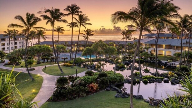 Ein Resort mit Poolbereich, Palmen und Blick auf den Ozean im Abendrot.