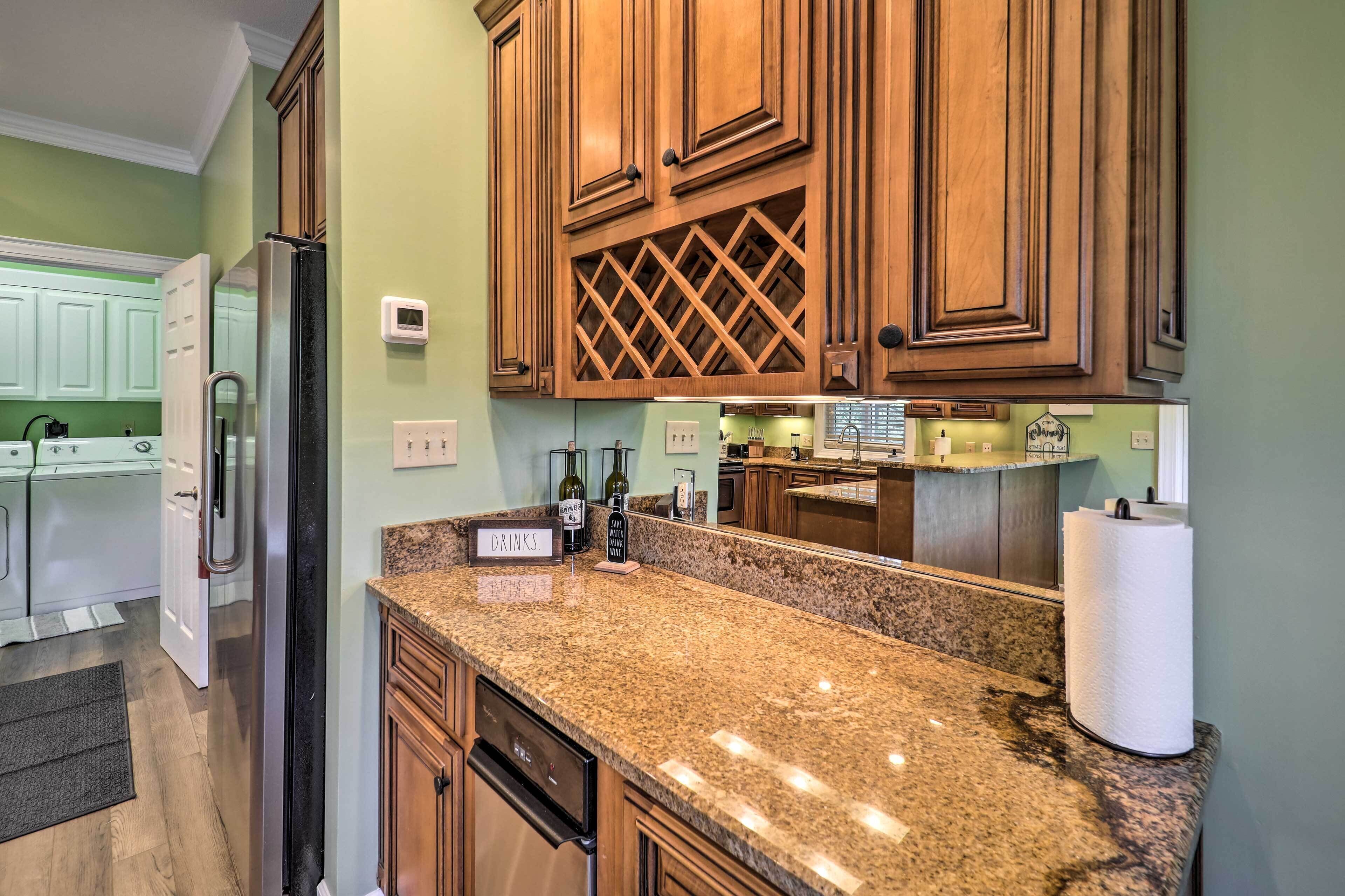 Una cocina con encimeras de granito, armarios de madera, un refrigerador de acero inoxidable y una botella de vino sobre la encimera.