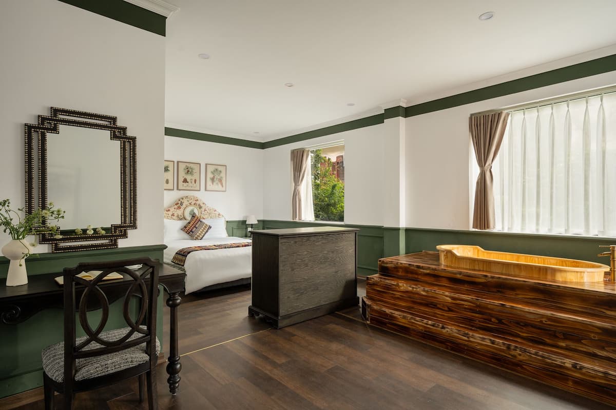 A room with a bed, a desk, a mirror, and a wooden bathtub.