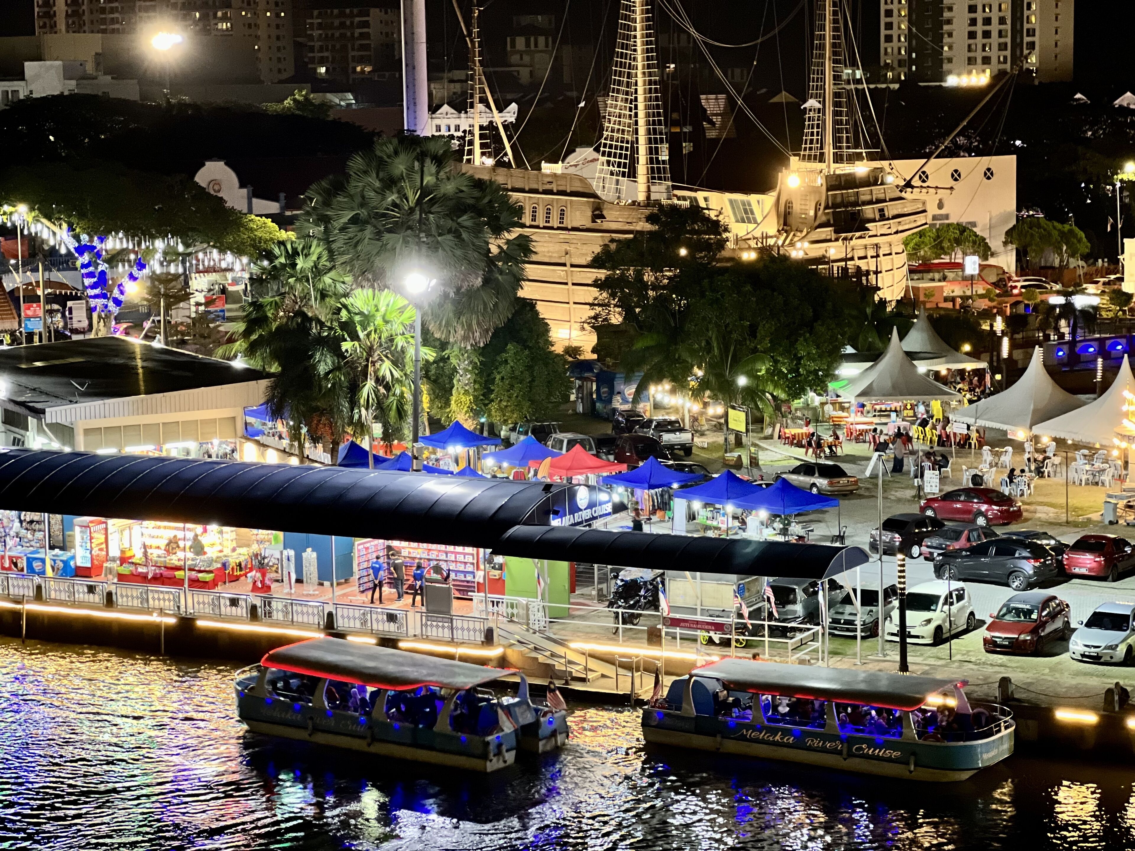 A nighttime waterfront area with boats, tents, and a bridge.