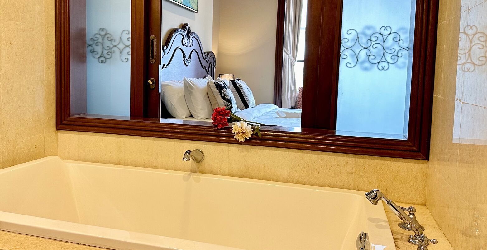 A bathroom with a large bathtub, a mirror above it, and decorative wall patterns.