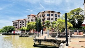 A waterfront building with multiple balconies, a paved walkway, and a canal. - Casa Del Rio Residence (Malacca City)