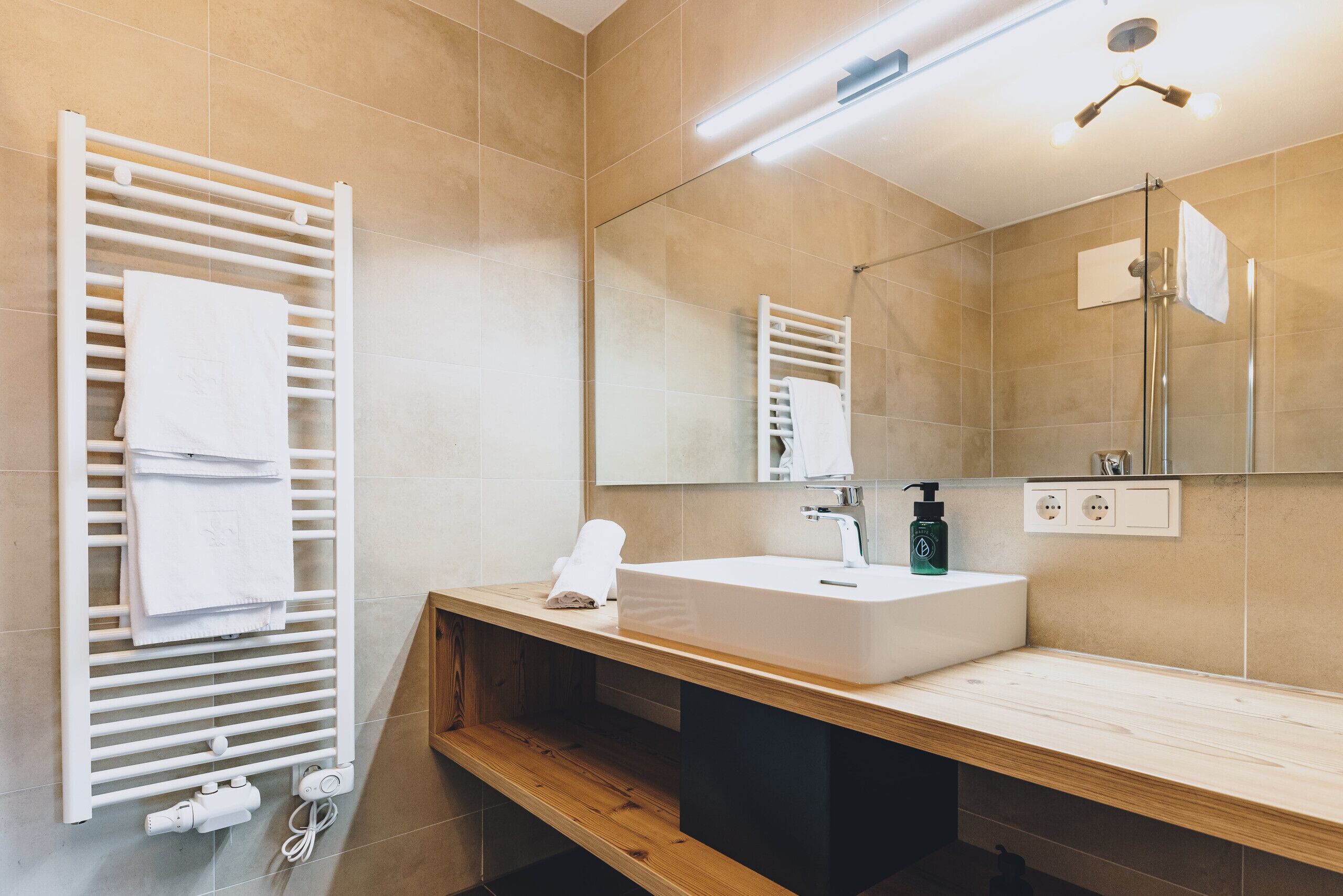 Un baño moderno con tocador de madera, lavamanos blanco, toallero y espejo.