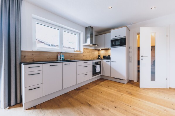 A modern kitchen with white cabinets, a wooden countertop, and a large window.
