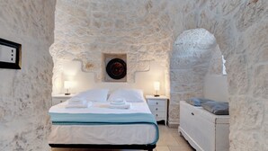 Un dormitori amb parets de pedra, un llit, taules de nit i una petita cambra amb calaixos.