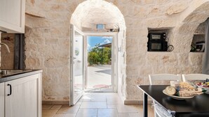 Cuina amb paret de pedra, una porta que dona a l'exterior i taula de menjador amb menjar.
