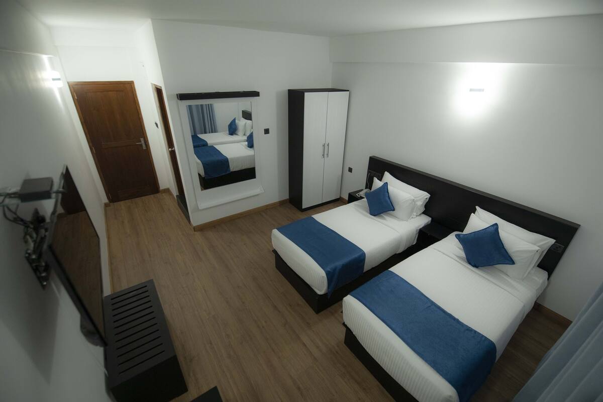 A hotel room with two beds, a wardrobe, a mirror, and a desk with a chair.
