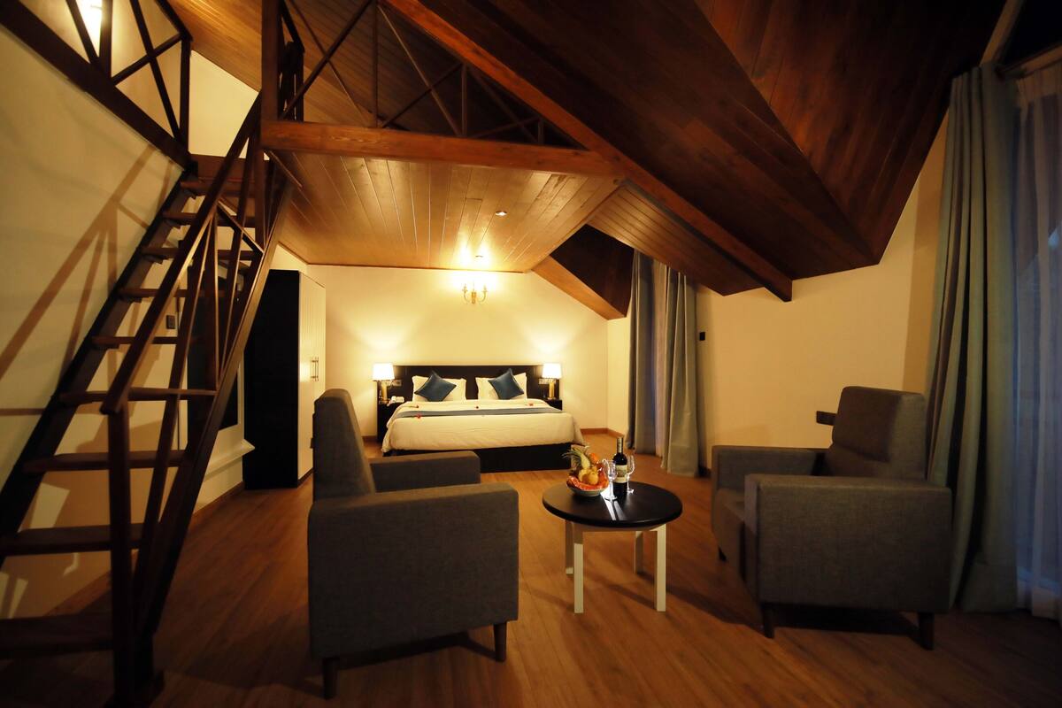 A hotel room with a lofted sleeping area, a staircase, and a seating area with a small table.