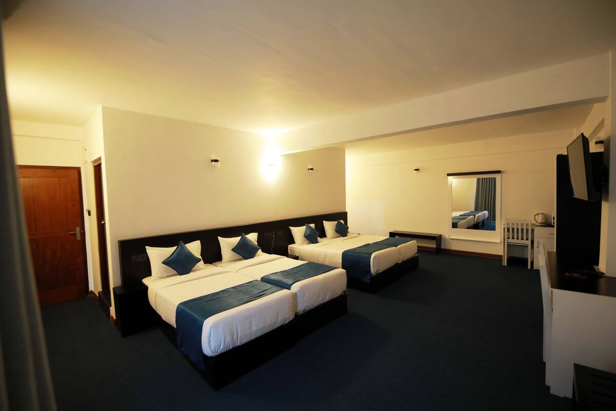 A hotel room with three beds, a desk, a chair, and a TV.
