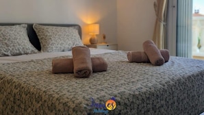 Una cama bien hecha con toallas enrolladas, una lámpara en la mesita de noche y una ventana con cortinas.