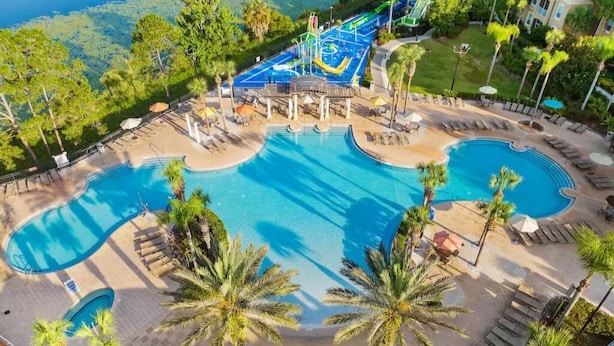 Área de piscina de un complejo turístico, con varias piscinas, palmeras y sillones de descanso.