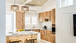 A modern kitchen with wooden cabinets, a marble countertop, and a central island with stools. - Seaside Escape Apartment Sea La View (Cape Town)