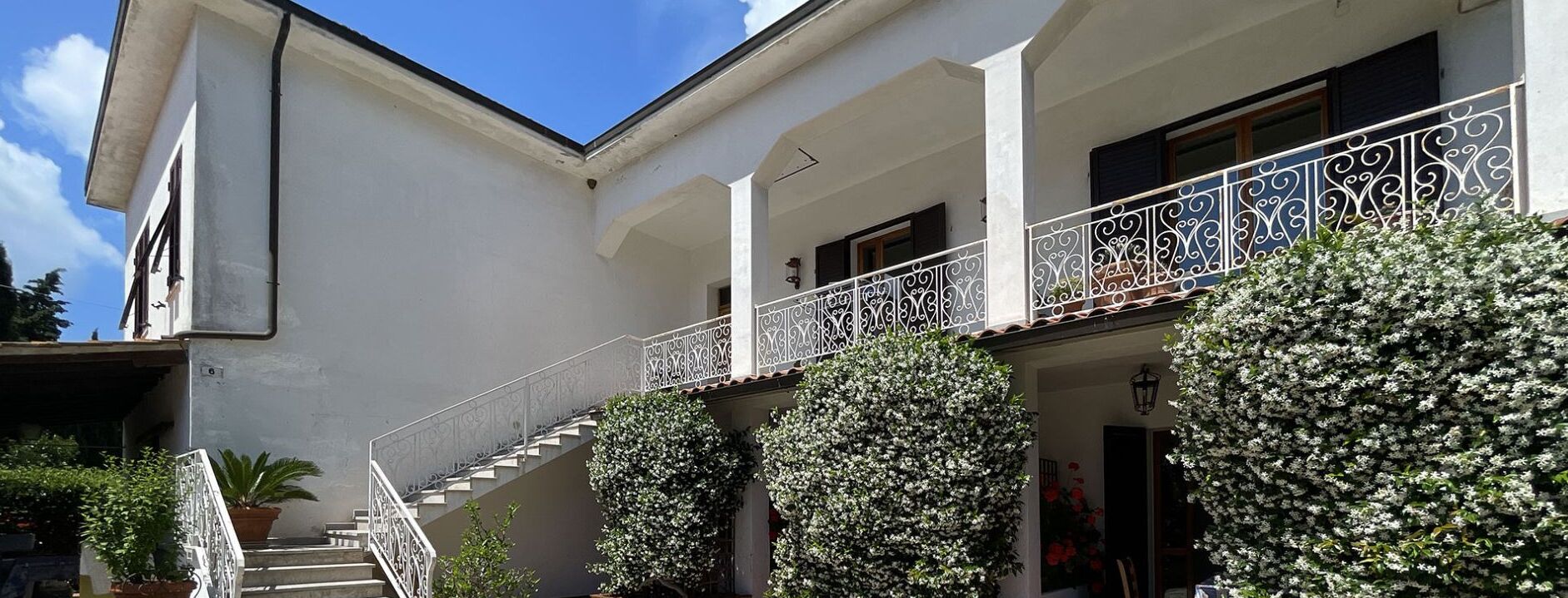 Um edifício com fachada branca, uma escadaria com grades brancas elaboradas e uma varanda com grades de metal decorativas.
