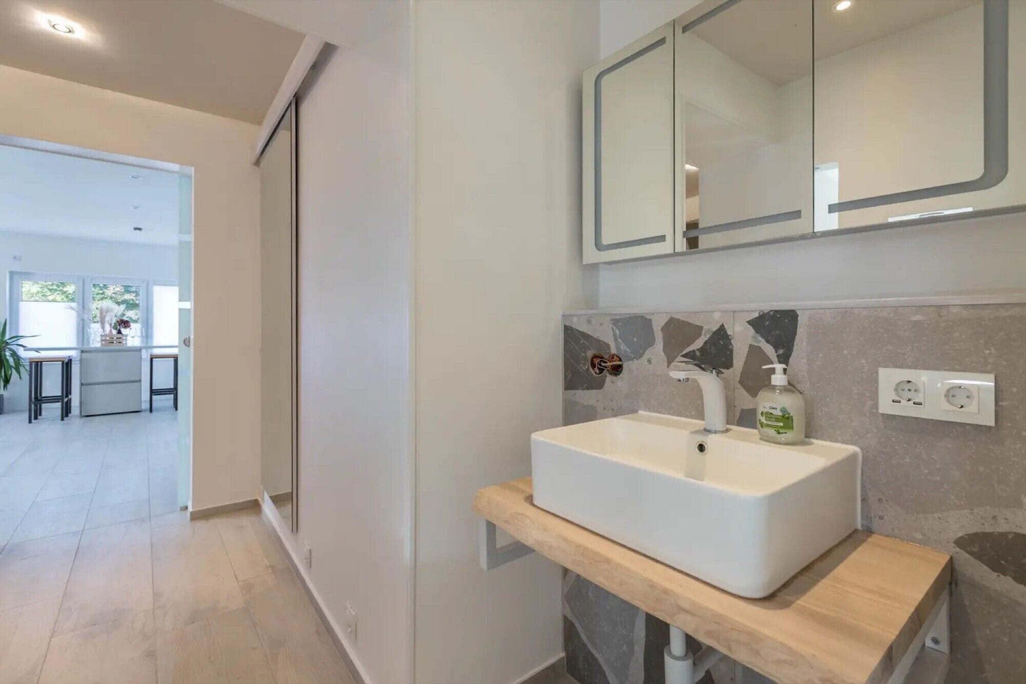 A modern bathroom with a white sink, a mirror above it, and a wooden countertop.
