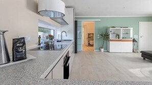 Una cocina moderna con estufa integrada, un ventanal grande y un comedor con un armario blanco y una planta.