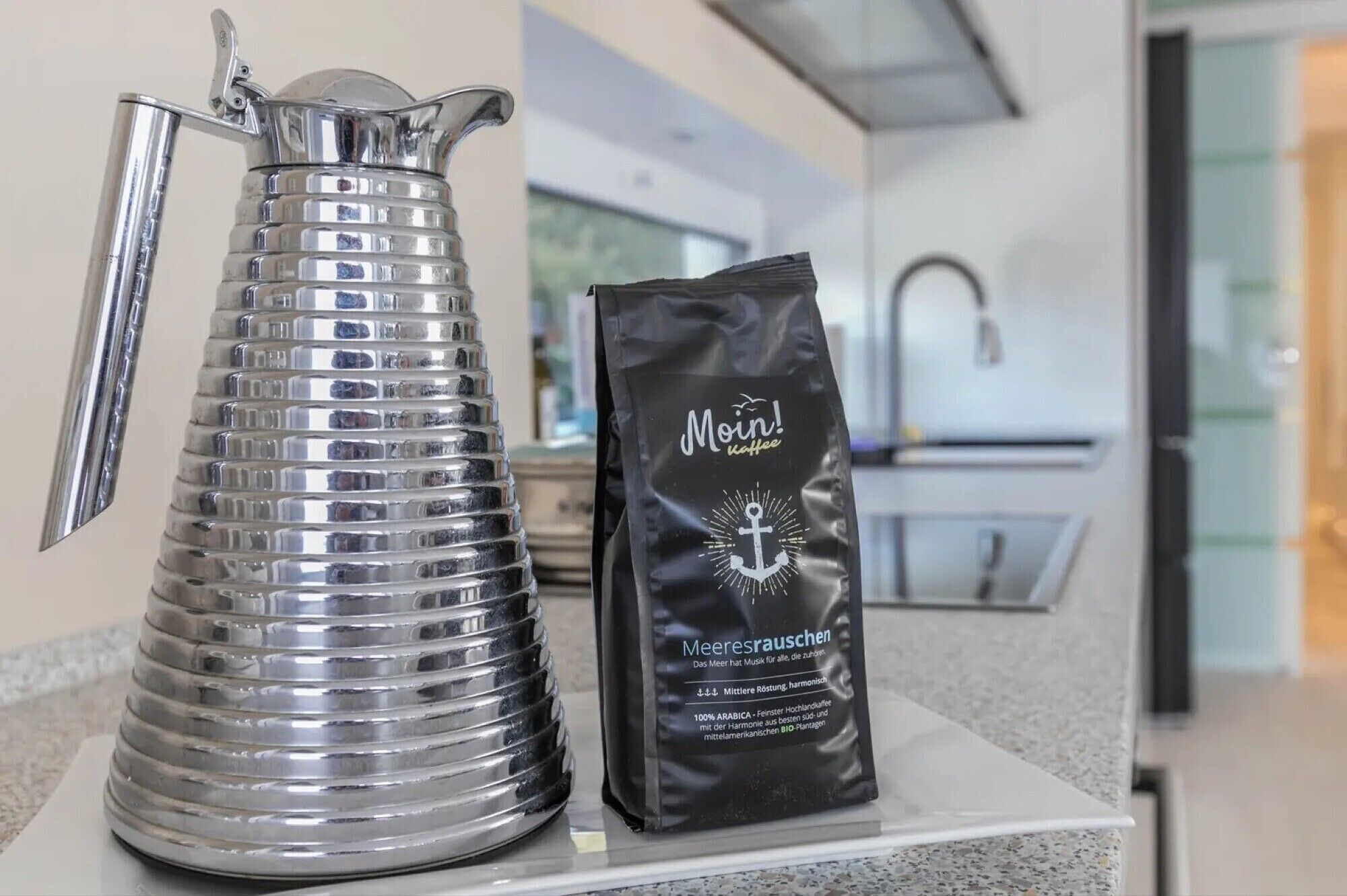 A stainless steel pitcher and a bag of coffee on a kitchen counter.