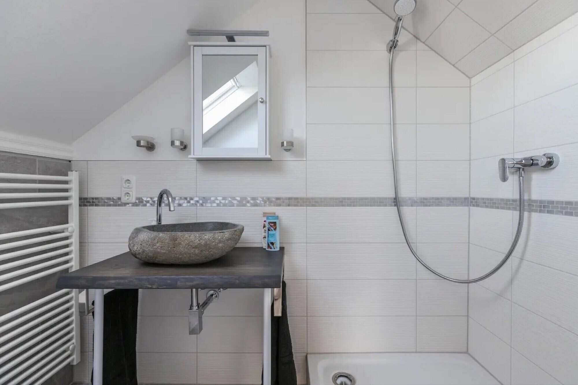 Une salle de bain avec un lavabo en pierre, une douchette à main et un miroir au-dessus du lavabo.