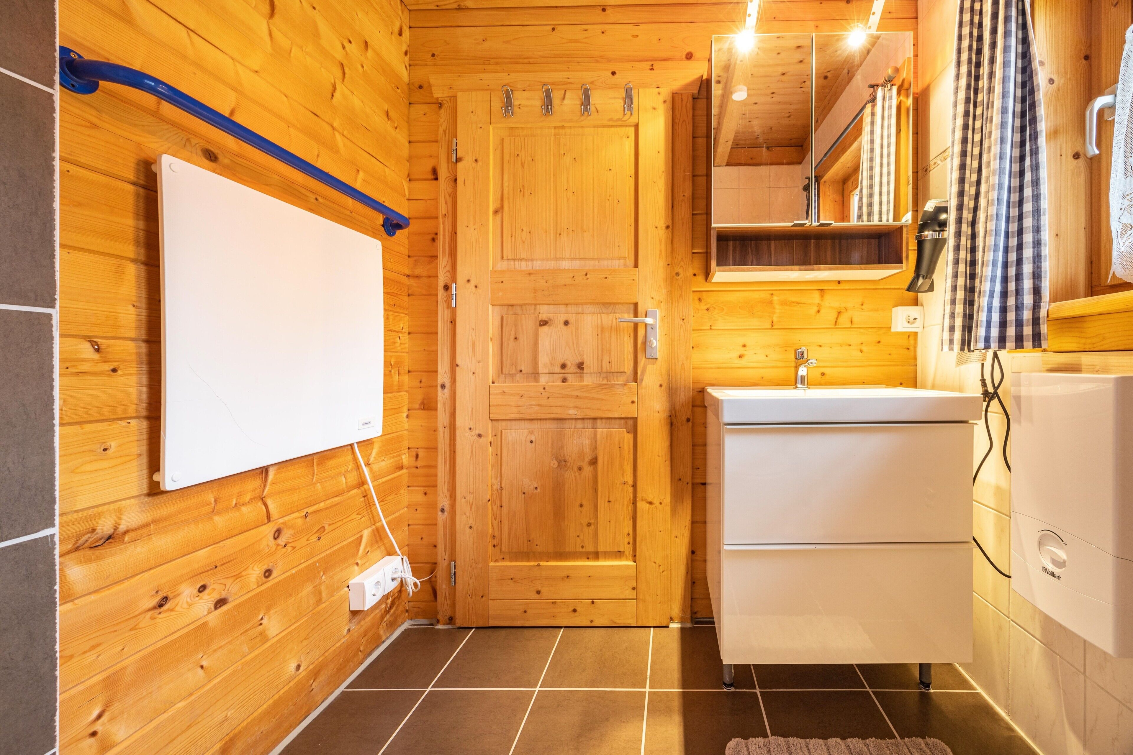 Interior de una cabaña de madera con un lavamanos blanco, un espejo, un perchero y una puerta.