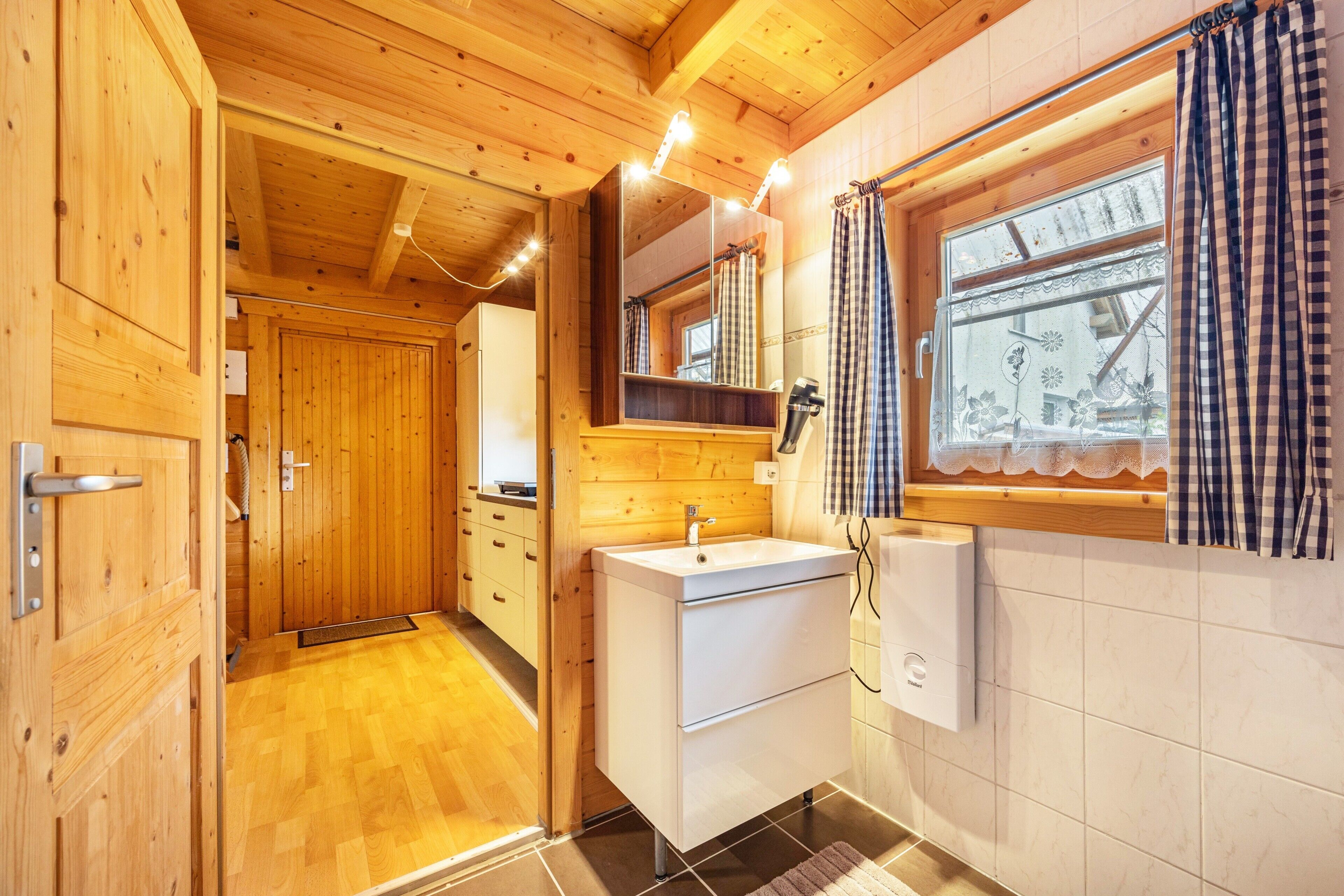 Un intérieur en bois avec une salle de bain comprenant un lavabo, un miroir et une fenêtre avec des rideaux.