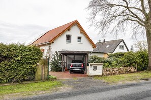Une maison à deux étages avec un garage, une voiture garée à l’intérieur et un mur de pierre à l’avant.