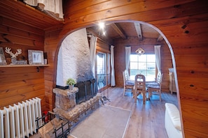 A log cabin interior with a stone fireplace, wooden dining table, and chairs.