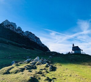 Un paysage montagneux avec un petit bâtiment en pierre situé sur une colline herbeuse.