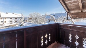 Uma varanda de madeira com árvores cobertas de neve e edifícios ao fundo.