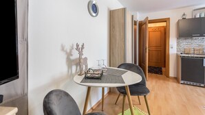 Um espaço de estar compacto com uma mesa redonda, duas cadeiras, uma televisão, um relógio, um armário de madeira e uma cozinha.