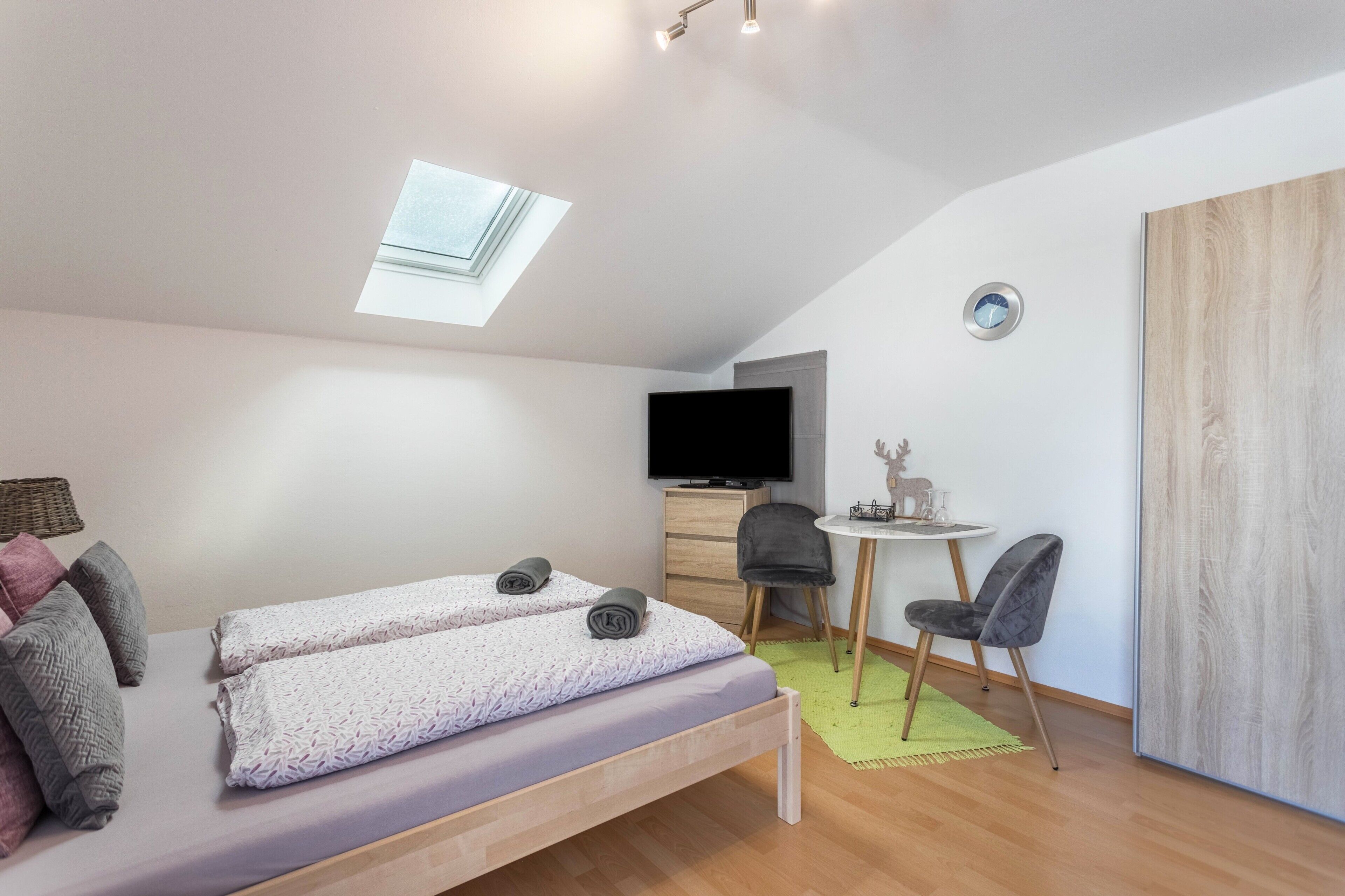 A compact room with a bed, a desk, a chair, a television, and a skylight.