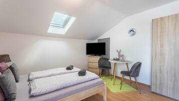 A compact room with a bed, a desk, a chair, a television, and a skylight.
