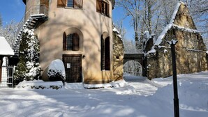 A snow-covered building with a stone archway, a metal staircase, and a snow-covered tree.