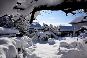 A snowy landscape with a wooden fence, snow-covered trees, and a building with a sloped roof.