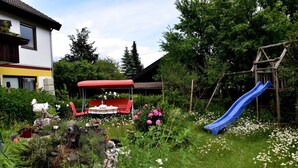 A garden with a red chair, a blue slide, and a house in the background.