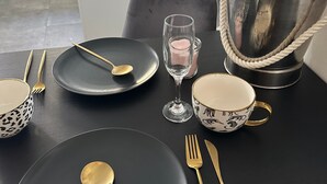 Une table à manger dressée avec des assiettes noires, des couverts dorés, un verre à vin et une tasse décorative.